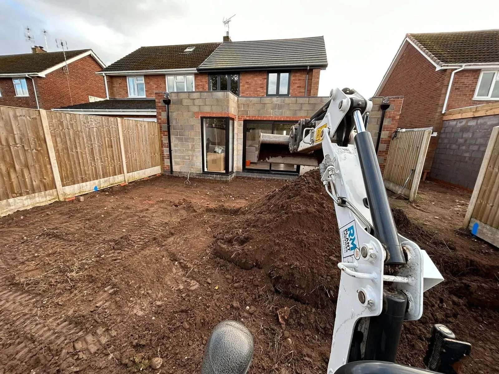 Blockwork rear extension shell with glazing fitted and a mini digger working in the garden